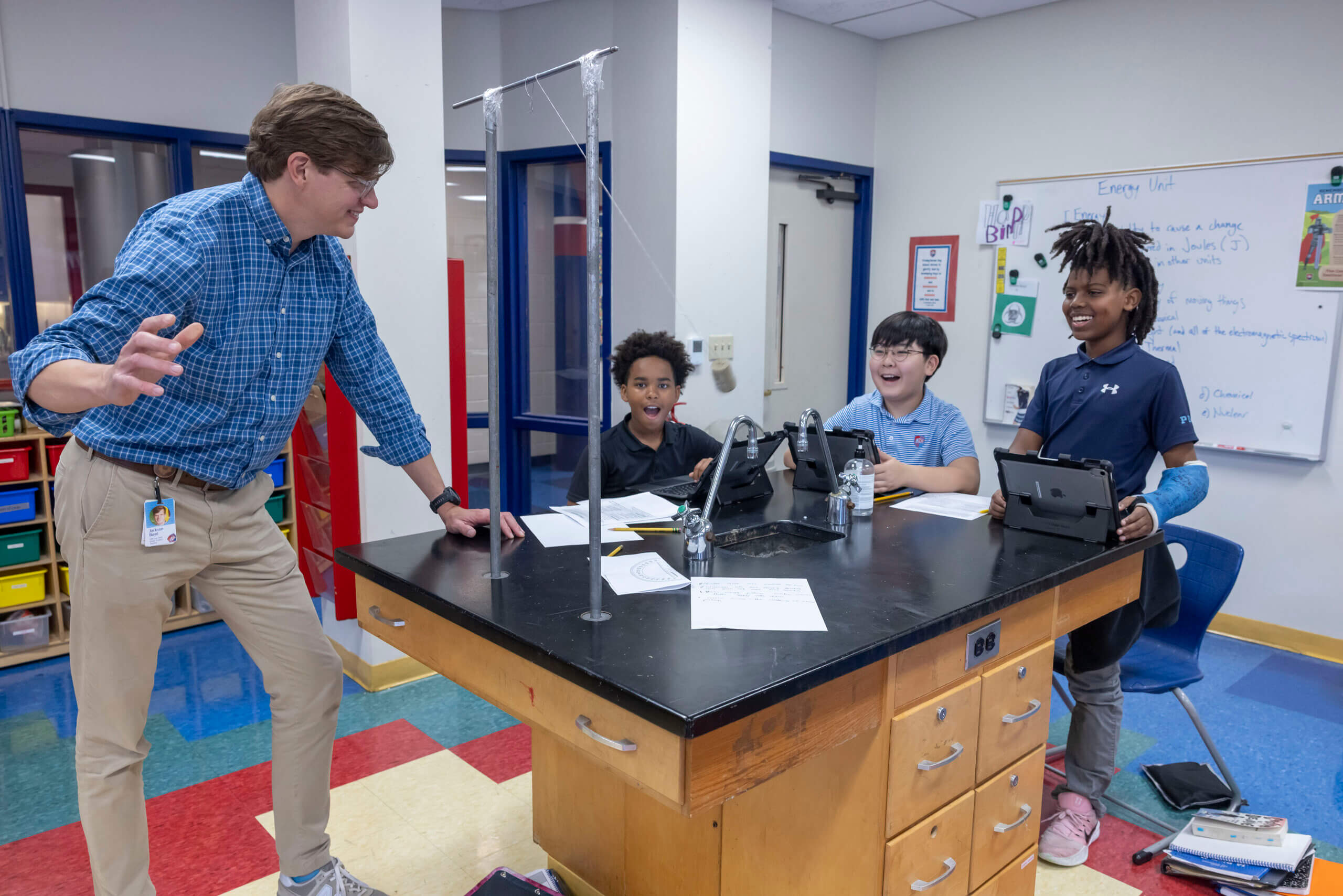 A teacher stands by a lab table as three students work on a science experiment with tablets and papers in a Memphis private school classroom.