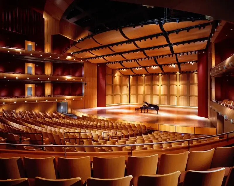 A modern, empty concert hall with wooden walls, tiered seating, and a grand piano on stage under warm lighting—perfect for hosting Live Theater Memphis events, including captivating musicals and plays.