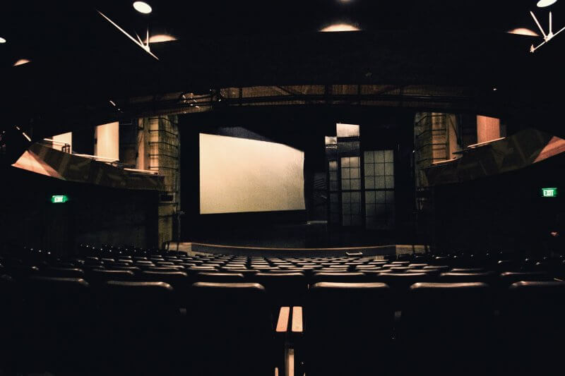 Empty theater auditorium with rows of seats facing a large white screen on stage, under dim lighting—an inviting space for experiencing captivating plays and musicals Memphis audiences love.