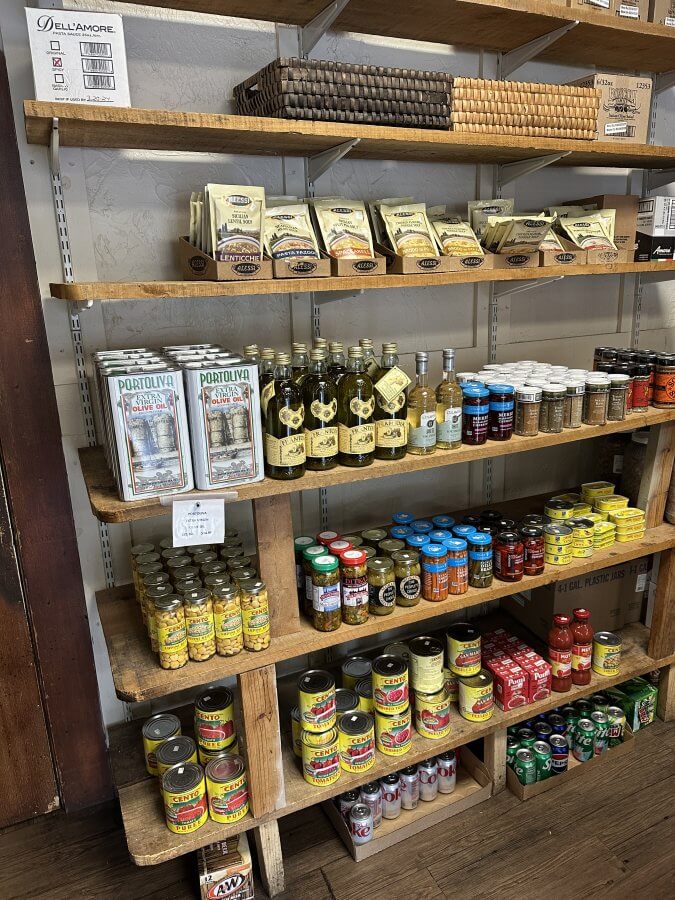 Memphis’s 10 Most Popular Articles of 2025 - 8 Wooden shelves stocked with various grocery items, including olive oil, canned tomatoes, spices, jars, and packaged foods in a small specialty market—a glimpse into the unique offerings found at Specialty Markets in Memphis.