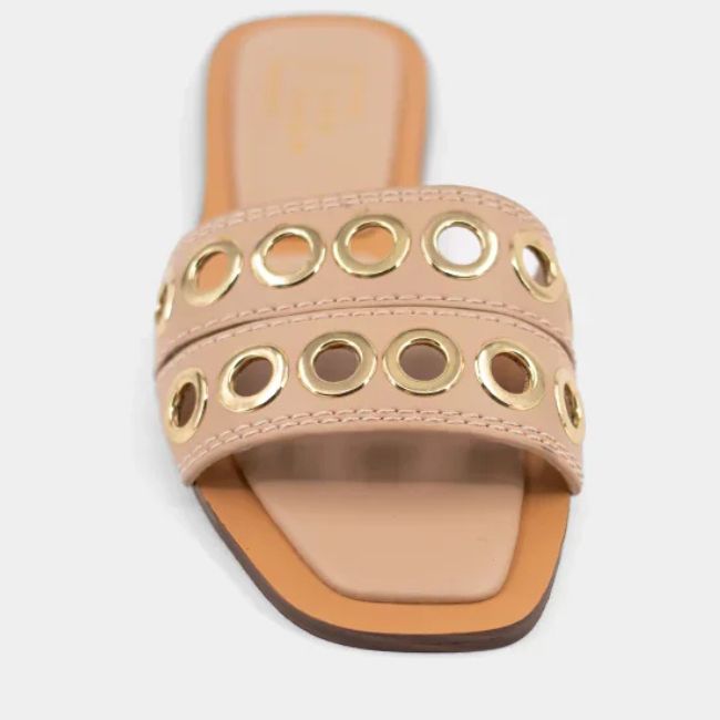 A beige slide sandal with two wide straps, each featuring gold metallic grommet accents and a stylish square toe design.