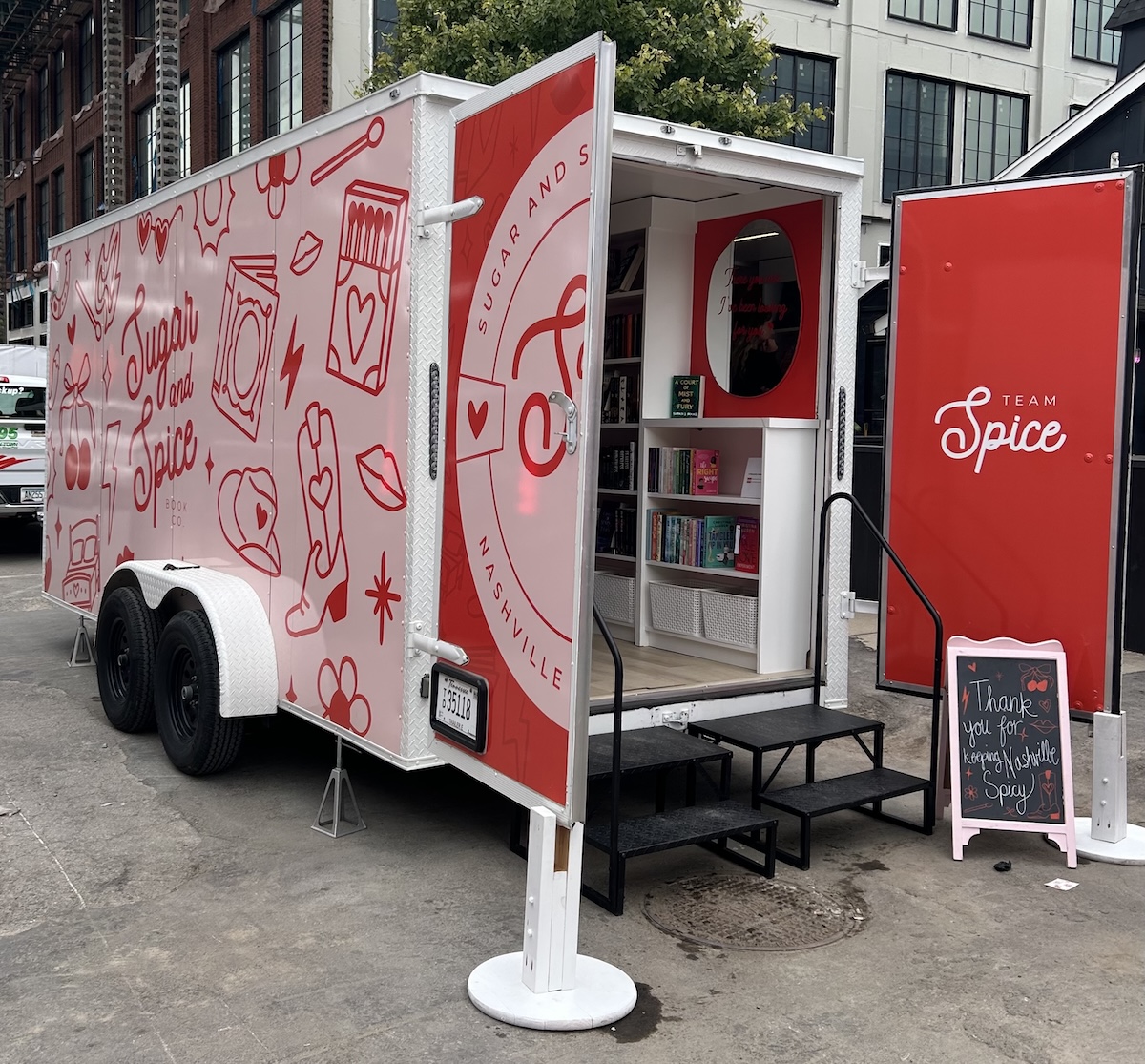 A red and white food truck with "Sugar & Spice Co" graphics is parked with its side open, displaying shelves of products and a sign that reads, "Thank you for your support." Catch it at Book Club Nashville events!.