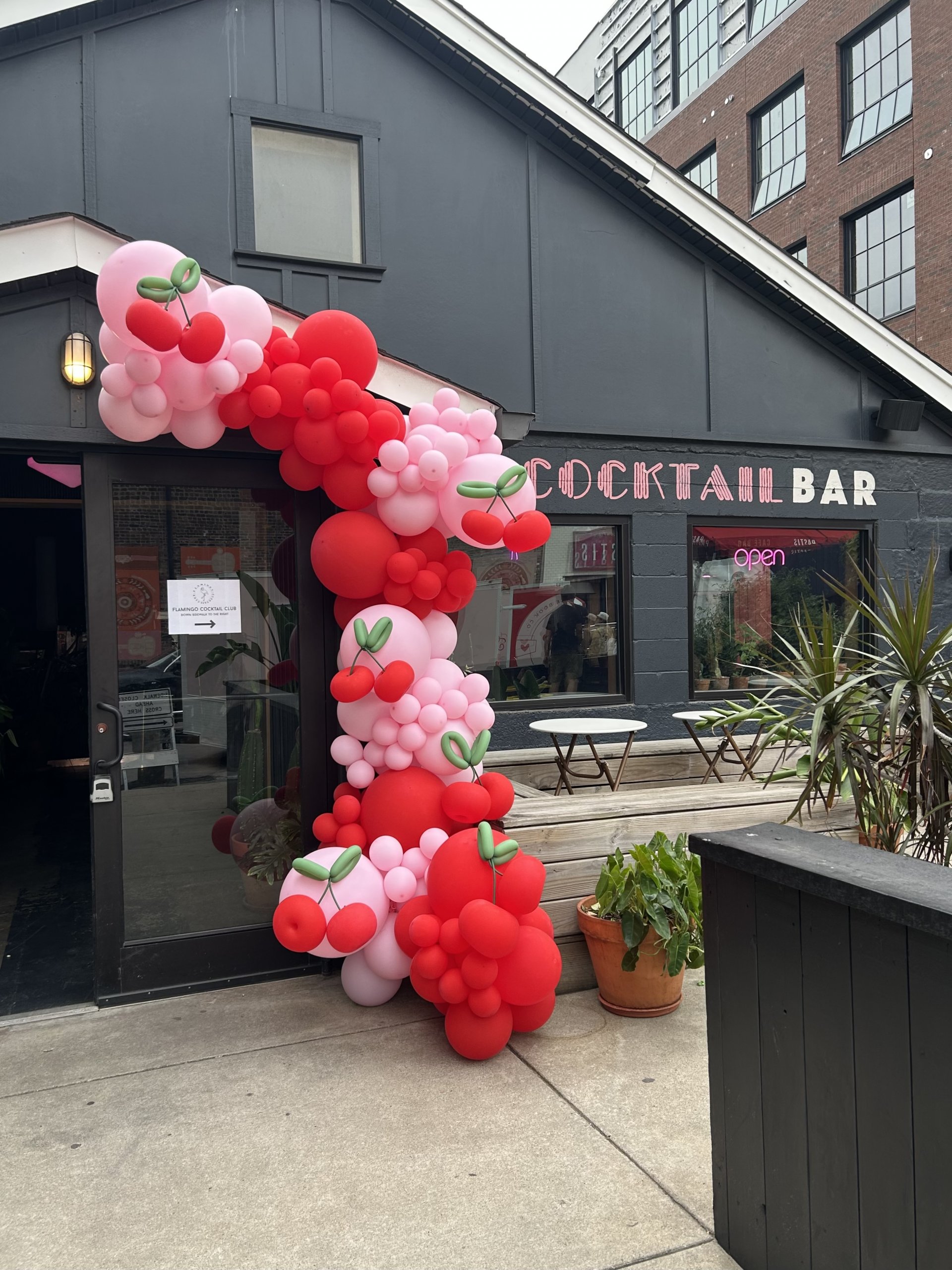 A cocktail bar exterior with a large balloon arch decoration in red and pink by Sugar & Spice Co., featuring cherry-shaped balloons at the entrance, perfect for a festive evening at Book Club Nashville.