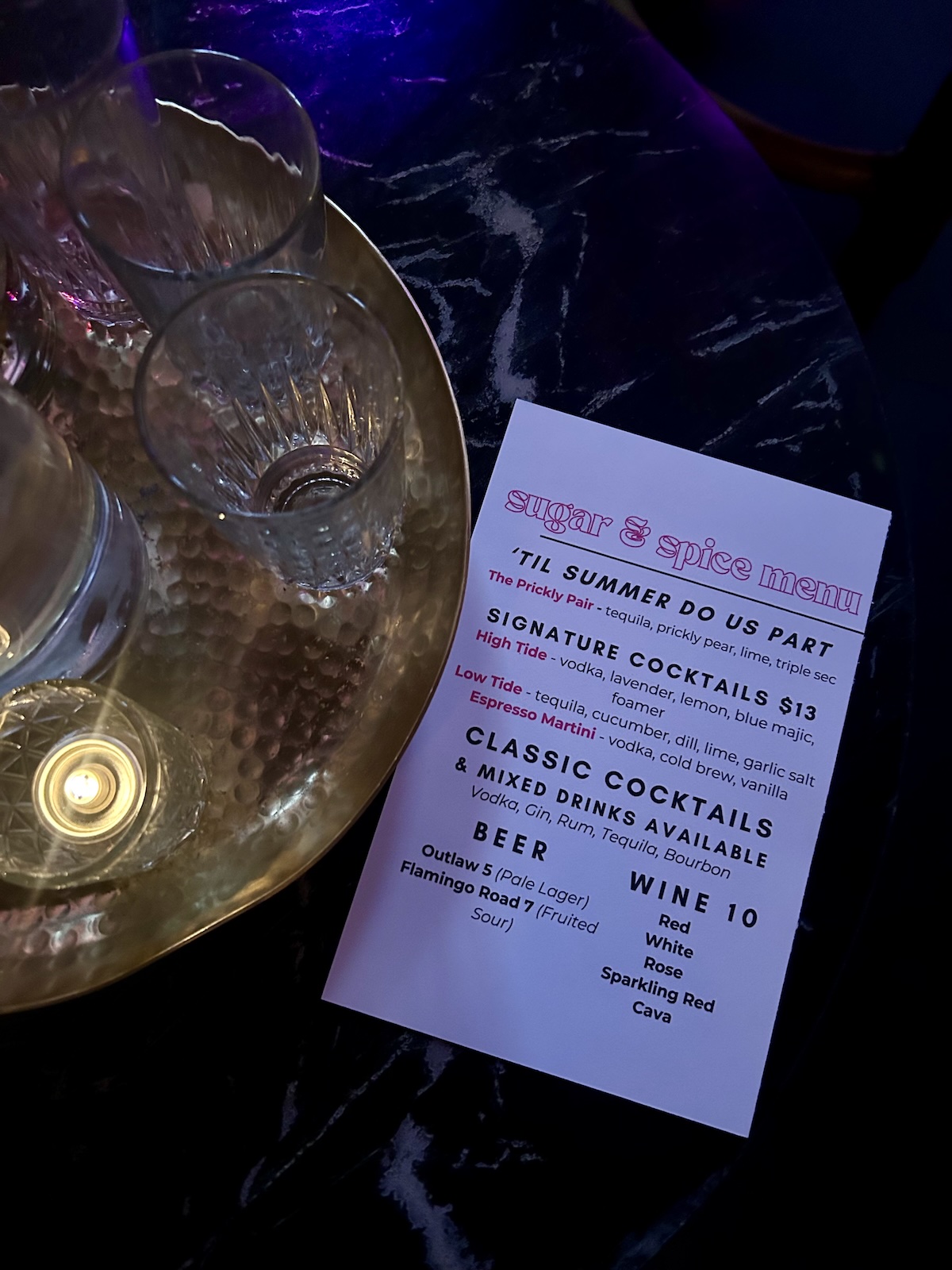 A dimly lit table with empty glasses, a candle, and a "sugar & spice menu" from Sugar & Spice Co. listing cocktails, classic drinks, and wine—perfect for your next Nashville book club gathering.