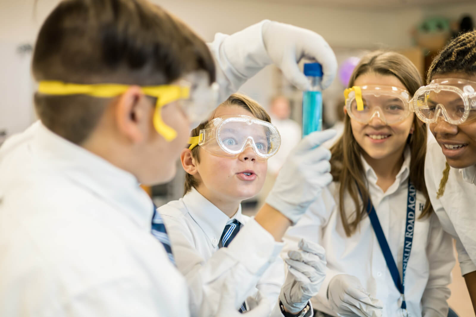 Nashville Private School Open House Dates - 3 Four students in school uniforms and safety goggles at a Nashville private school observe a test tube with blue liquid during a science experiment in a classroom.
