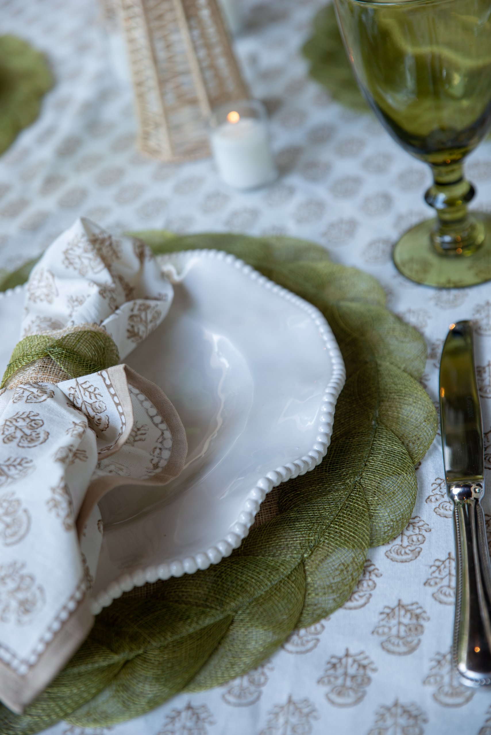 A patterned tablecloth with green placemat and luxury green-themed table sedtting