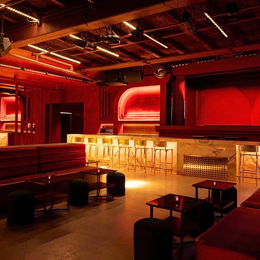 A modern lounge in downtown Nashville with red walls, gold barstools, marble bar counter, and ambient lighting; perfect spot for your next event or a night out at High Notes & Highballs. Empty seating and tables are visible.