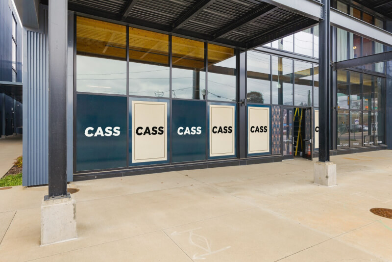 A commercial building exterior with large windows and five panels, each boldly displaying the word "CASS."
