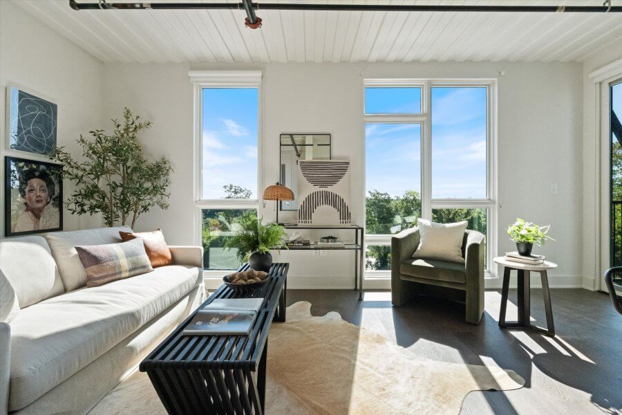 Bright living room at 2126 Byrum Ave, Nashville TN, featuring large windows, a white sofa, green armchair, coffee table, indoor plants, and modern art. Sunlight streams in, illuminating the stylish space.