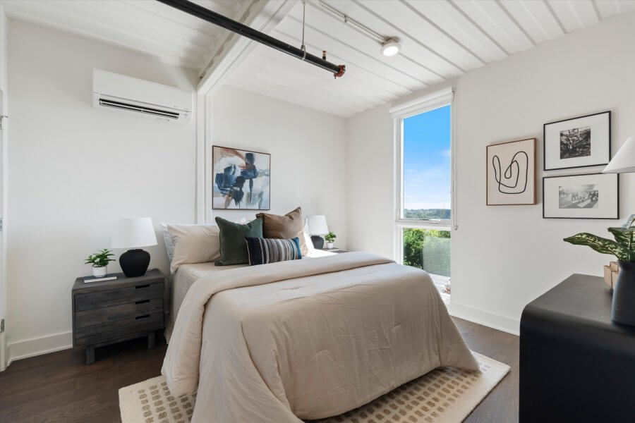 Modern bedroom in Nashville TN featuring a neatly made bed, nightstands, lamps, framed wall art, large window with a view, and a dresser with decorative objects—an inviting retreat at 2126 Byrum Ave.