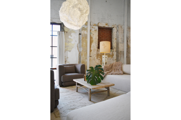 A modern living room with neutral sofas, a wooden coffee table featuring a large green leaf centerpiece, and exposed, weathered walls. Don’t miss our Once a Month Sale on unique pendant lights to elevate your space.
