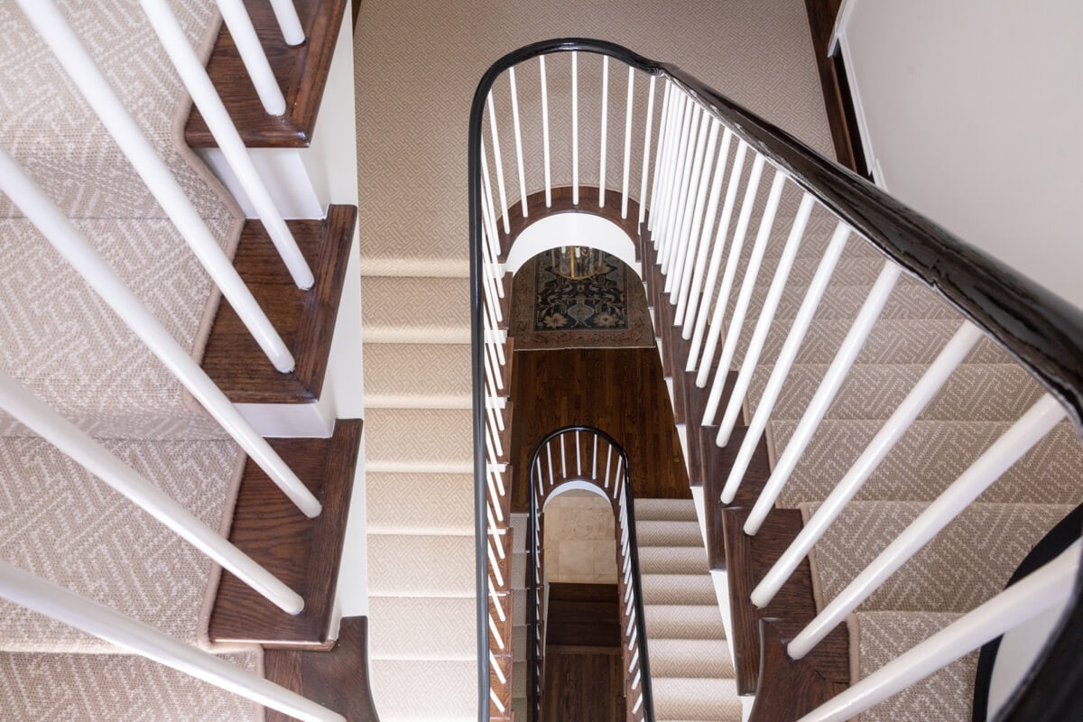 A top-down view of a spiral staircase with white railings, dark wooden handrails, and beige carpeted steps inside a Buckhead home in Atlanta.