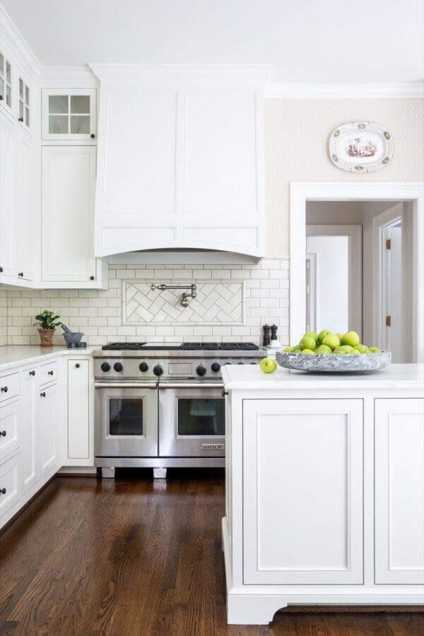 A modern white Buckhead kitchen with a stainless steel stove, a bowl of green apples on the island, subway tile backsplash, and hardwood floors.