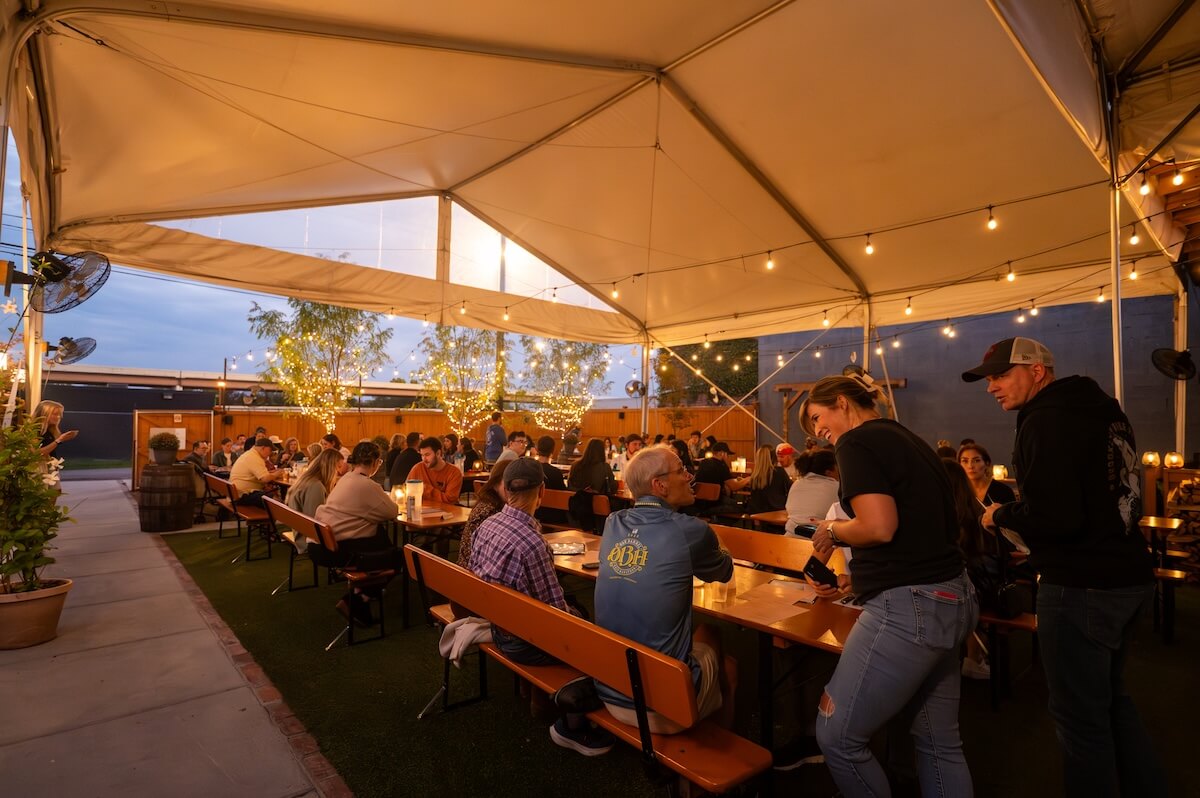 People enjoy local favorites at wooden tables under a large white canopy with string lights and small trees, discovering a cozy outdoor evening restaurant setting in Nashville.