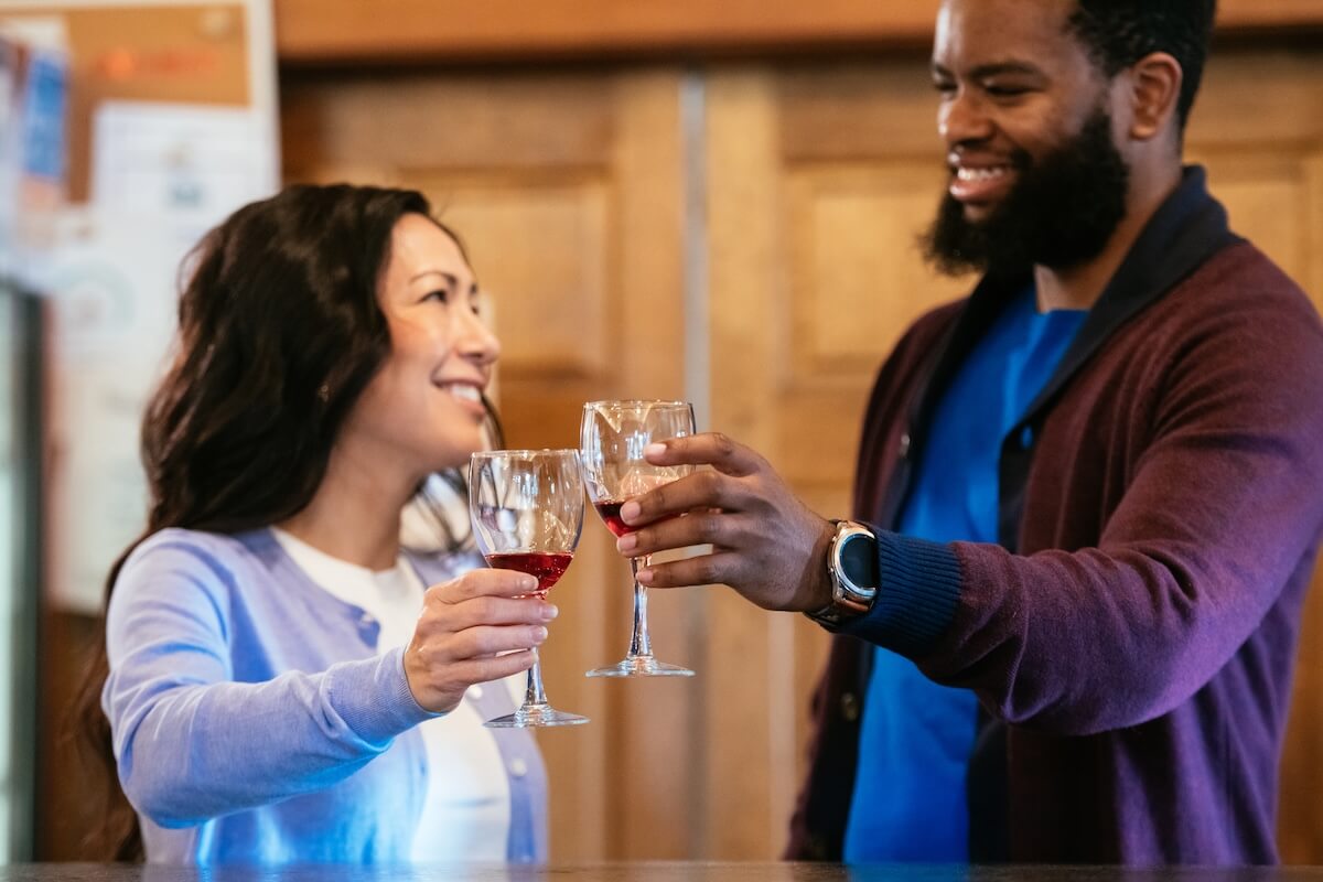 Culinary Road Trip: 4 Tennessee Towns for Food Lovers - 8 Two food lovers stand indoors, smiling and clinking wine glasses together, toasting to their latest culinary road trip in Tennessee.