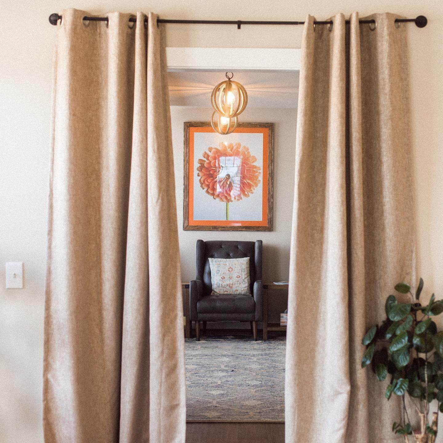 She’s Behind Two of Birmingham’s Most Beloved Day Spas - 5 Cream-colored curtains frame a view into a tranquil room with an armchair, patterned pillow, framed flower artwork, rug, plant, and hanging light at The Retreat Day Spa.
