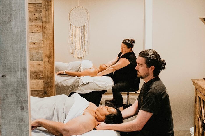 She’s Behind Two of Birmingham’s Most Beloved Day Spas - 3 At The Retreat Day Spa, two people unwind at one of the city's top day spas, receiving massages from expert therapists in a calm, softly lit room adorned with wooden accents and a dreamcatcher on the wall.