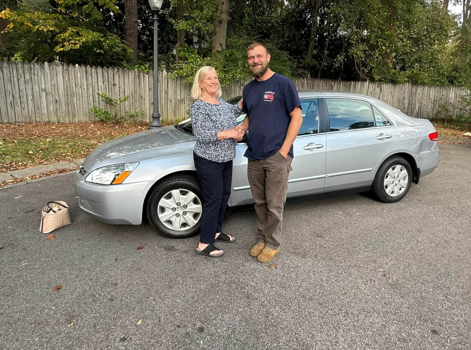 How 'Three Hots and a Cot' is Supporting Birmingham Veterans - 8 A woman and man stand in front of a silver sedan shaking hands to commemorate the donation of a vehicle to a veteran through Three Hots and a Cot.
