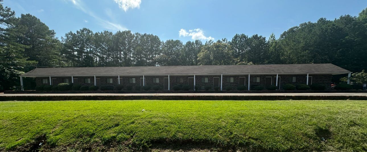 How 'Three Hots and a Cot' is Supporting Birmingham Veterans - 7 A single-story brick building with multiple doors and windows, surrounded by trees and a grassy lawn under a clear sky.
