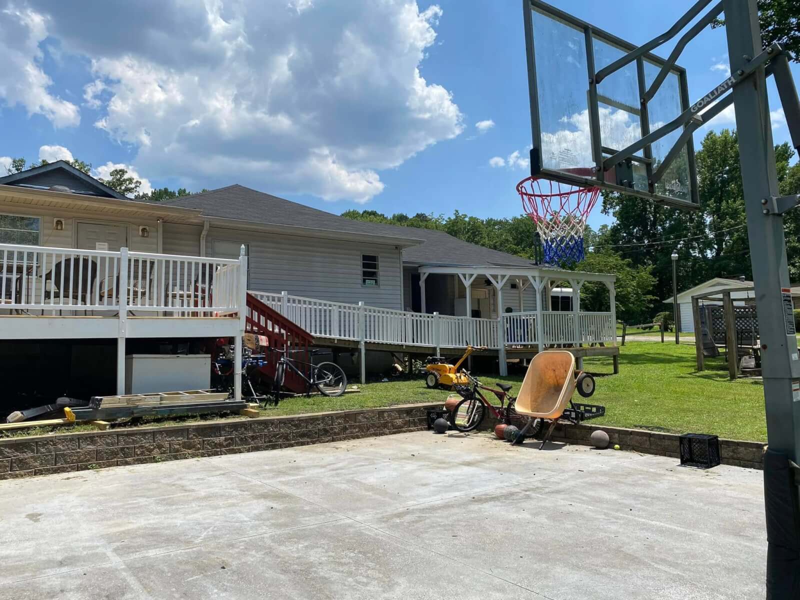 How 'Three Hots and a Cot' is Supporting Birmingham Veterans - 5 A backyard with a basketball hoop, concrete court, and various yard tools and bicycles near a white house with a porch and ramp.