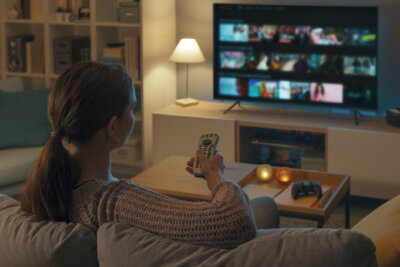 A woman sits on a couch, pointing a remote at a television screen displaying a menu of southern gothic movies.