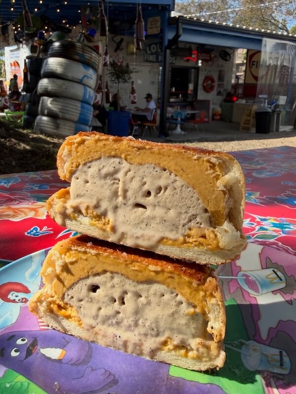 A sandwich bun cut in half, filled with ice cream and a layer of orange filling, sits on a colorful cartoon-themed plate outdoors near a retro-themed building—perfect for exploring unique treats found on Nashville fall menus.