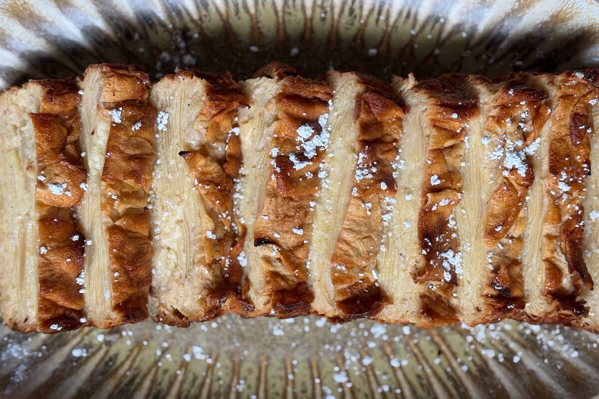 Sliced Invisible French Apple Cake topped with powdered sugar, arranged on a patterned plate.