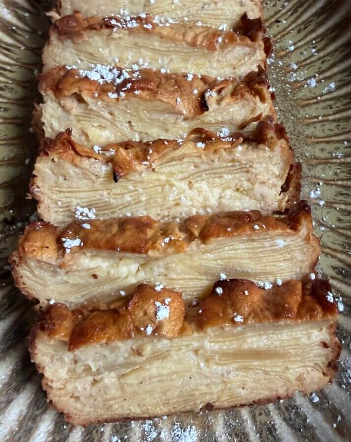 RECIPE: Invisible French Apple Cake - 6 Five slices of Invisible French Apple Cake are arranged in a row on a patterned platter, each dusted lightly with powdered sugar.