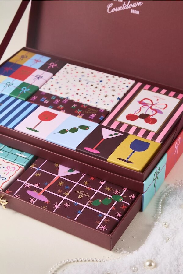 The BEST Advent Calendars for 2025 - 23 A box of assorted chocolates with colorful, patterned wrappers, arranged neatly in rows inside an open burgundy box—perfect as a sweet treat or for filling 2025 Advent Calendars.