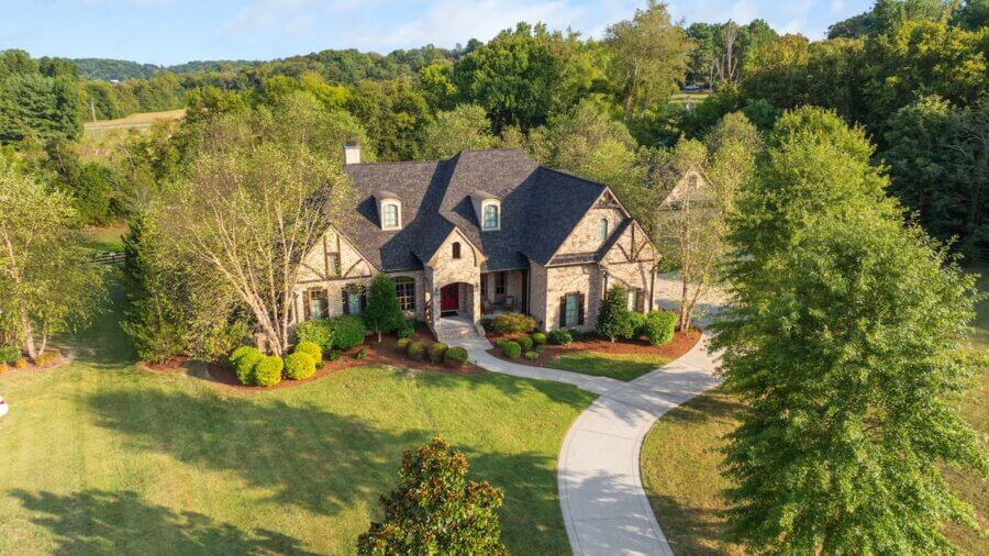Just Listed! A Franklin Home Where Style & Serenity Coexist - 17 A large stone Franklin Home with a dark roof sits on a spacious, landscaped lot with a curved driveway, surrounded by trees—perfect for those seeking Luxury Living and pastoral peace.