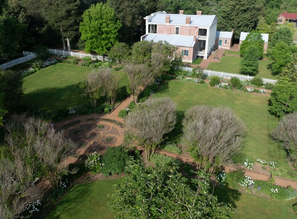 Aerial view of a large historic house in Nashville with a white fence, gardens, circular walkway, manicured lawns, and surrounding trees—perfect for discovering local favorites and hidden gems.