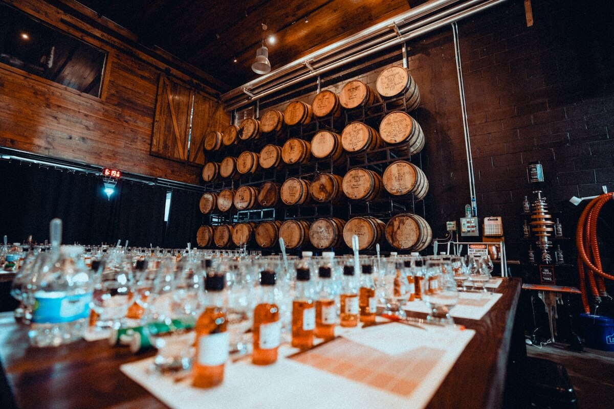 Discovering Nashville’s local favorites, wooden barrels are stacked in a distillery with a table in the foreground holding glass bottles, droppers, and papers for tasting or testing.