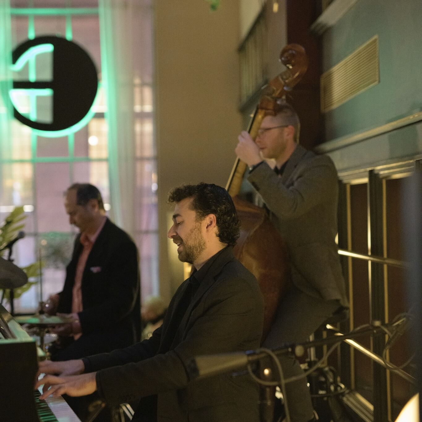 Three musicians perform indoors; one plays piano, another upright bass, and the third stands behind them. Dressed formally and focused, they embody the vibrant music scene found among top Nashville attractions.