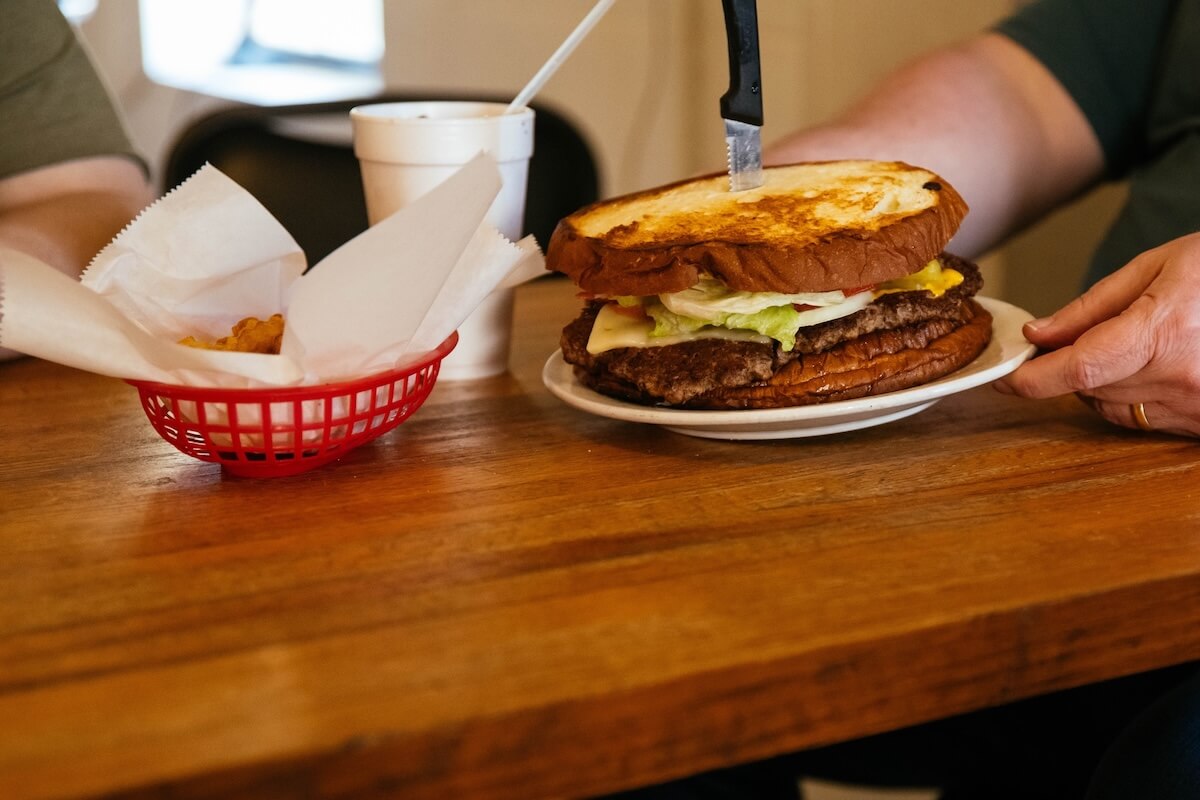 5 Beloved Tennessee Destinations for Adventure Lovers - 7 A large double cheeseburger with a knife in the bun sits on a plate next to tater tots and a cup—perfect fuel before heading out to explore Tennessee outdoor escapes or nearby adventure towns.