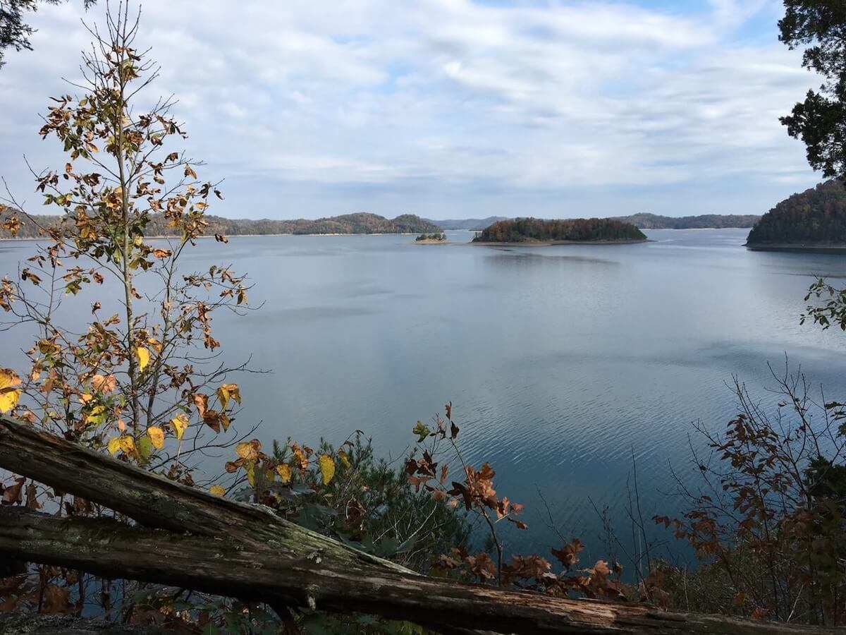 5 Beloved Tennessee Destinations for Adventure Lovers - 6 A calm lake with small tree-covered islands under a partly cloudy sky, framed by autumn foliage and tree branches in the foreground—a perfect scene for Tennessee outdoor escapes and peaceful Tennessee travel.