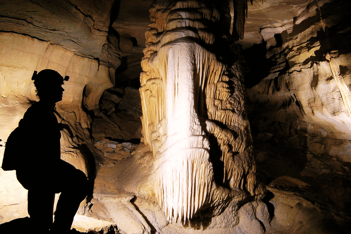 5 Beloved Tennessee Destinations for Adventure Lovers - 9 A person wearing a helmet stands in silhouette inside a cave, facing a large, illuminated stalagmite formation—a perfect scene from one of many Tennessee adventure towns ideal for unforgettable outdoor escapes.