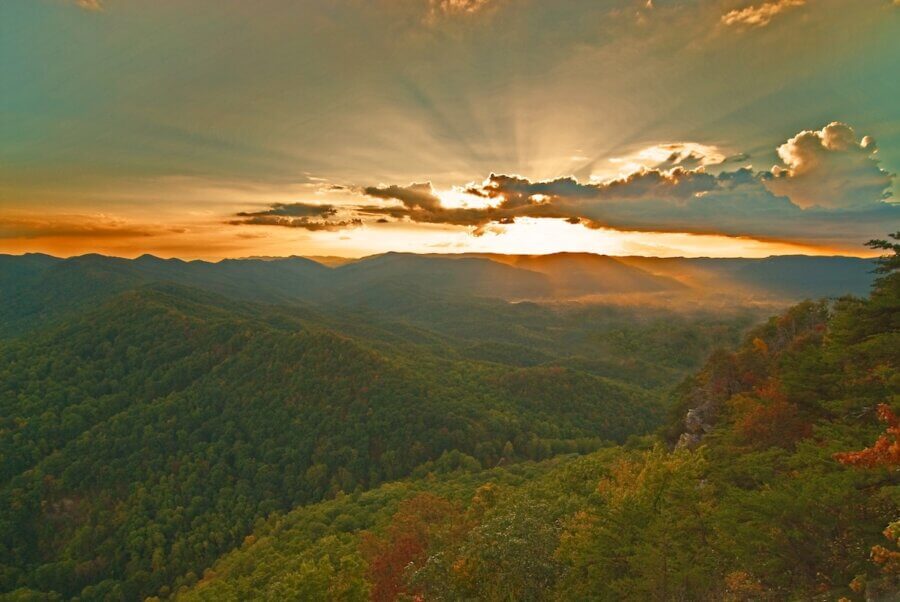 5 Beloved Tennessee Destinations for Adventure Lovers - 11 Sunset over rolling, forested mountains in Tennessee, with rays of sunlight streaming through clouds—an inspiring scene for outdoor adventures, illuminating the breathtaking landscape below.
