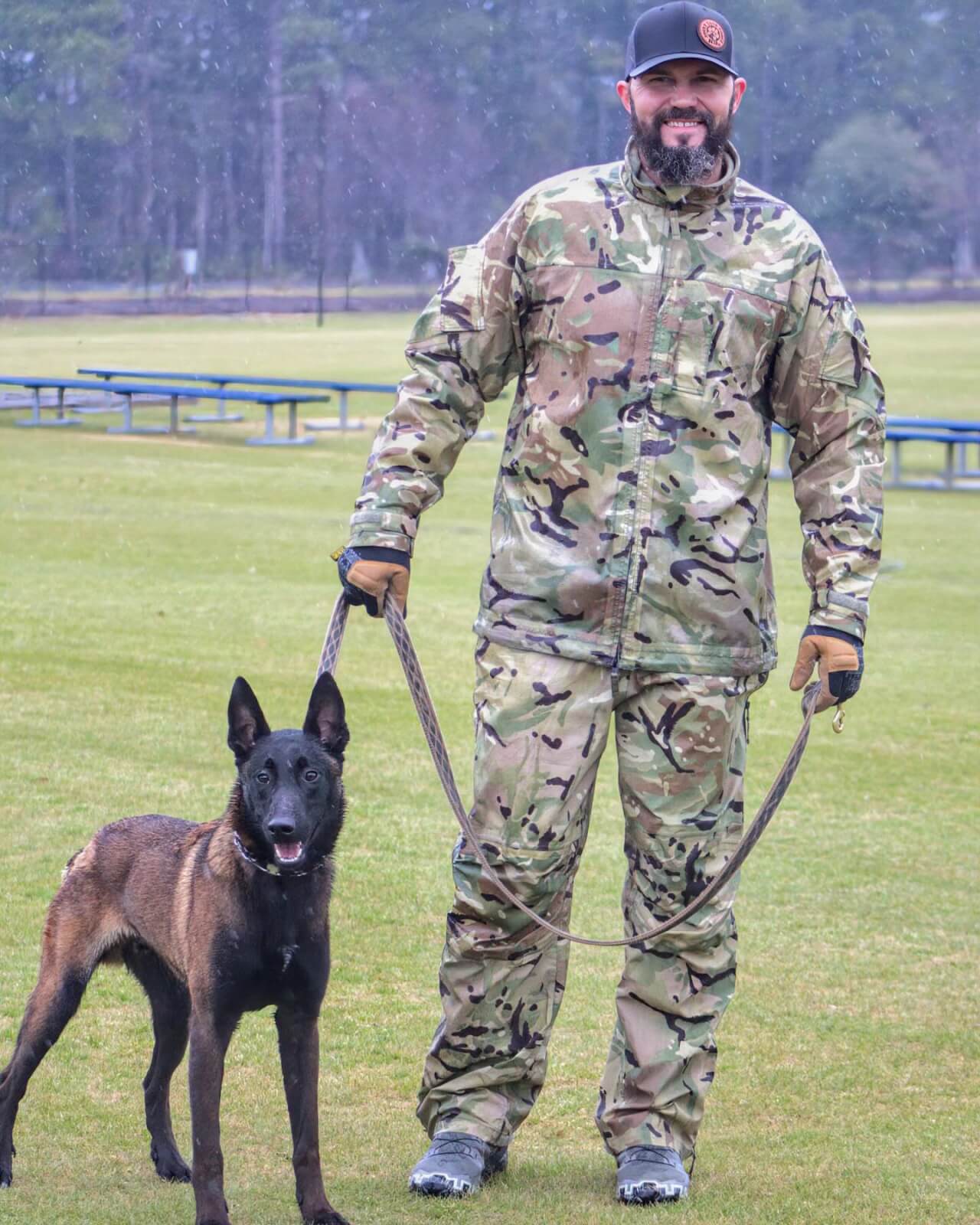 6 Organizations Pairing Canines and Veterans Across the South - 8 Keith Holland wearing camouflage clothing stands on grass holding the leash of a Belgian Malinois. a service dog with Joint Task Force K9s.