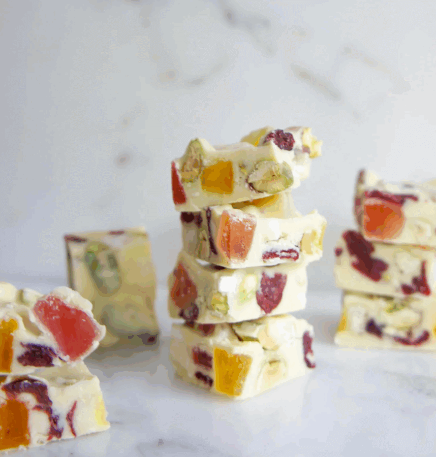 50 Under $50: Your BHAM Holiday Gift Guide - 35 Three stacks of white chocolate bark with dried fruit and nuts sit on a white marble surface—an elegant treat perfect for any Holiday Gift Guide in Birmingham for 2025, with extra pieces scattered invitingly nearby.