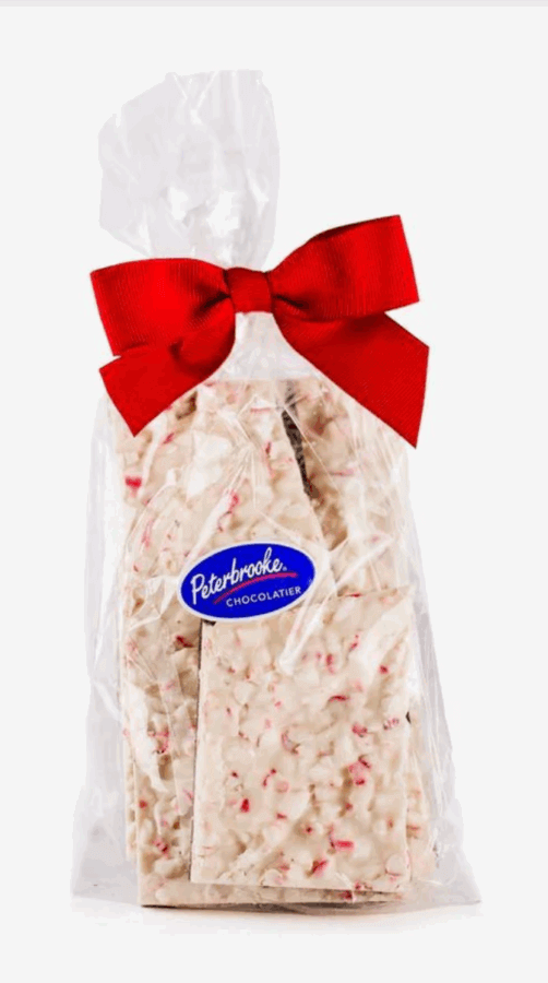 50 Under $50: Your BHAM Holiday Gift Guide - 38 A clear plastic bag of white chocolate peppermint bark with a red bow and a Peterbrooke Chocolatier label—perfect for holiday gifts or as a sweet addition to the Birmingham Holiday Gift Guide.