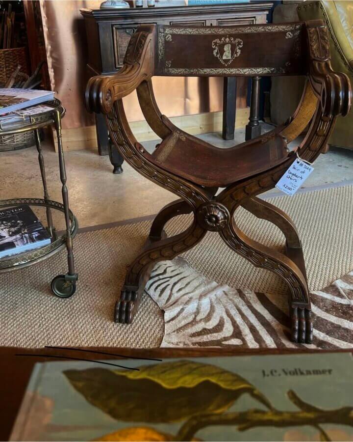 19 Luxurious Birmingham FINDS for the Holidays - 14 Ornate wooden Renaissance-style chair with clawed feet, placed on a rug beside a small table with magazines in a warmly lit, luxurious room—perfect for relaxing during the holidays or entertaining guests in Birmingham.