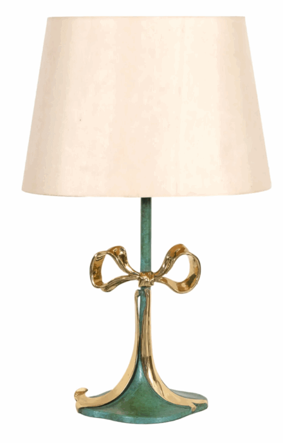 19 Luxurious Birmingham FINDS for the Holidays - 15 A table lamp with a beige tapered lampshade and a metallic gold bow-shaped accent on a green and gold base—a perfect luxurious Birmingham find to elevate your home décor.