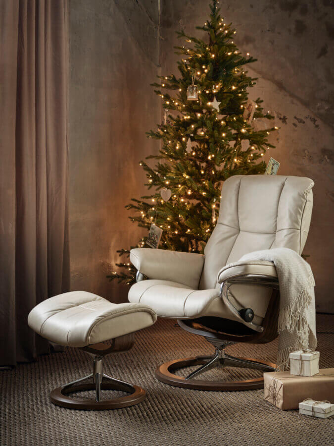19 Luxurious Birmingham FINDS for the Holidays - 13 A beige armchair with matching footrest sits near a decorated Christmas tree, surrounded by holiday gifts and a blanket draped over the chair—creating a cozy, softly lit space perfect for those luxurious Birmingham winter evenings.