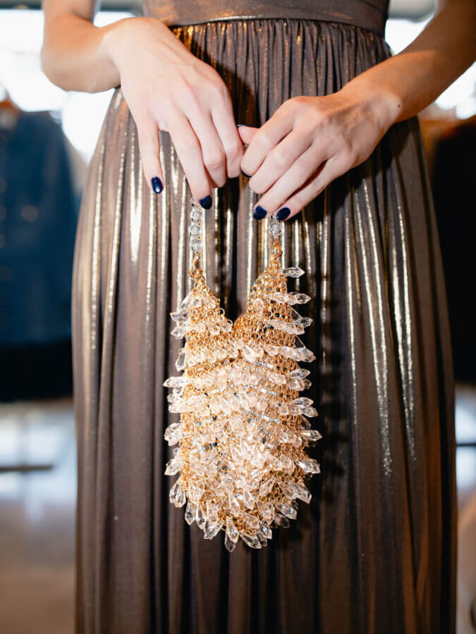 3 BHAM Boutiques Share Their Favorite Holiday Looks - 5 A person in a metallic pleated dress holds a gold and crystal beaded handbag with both hands—perfect inspiration for holiday looks from Birmingham boutiques.