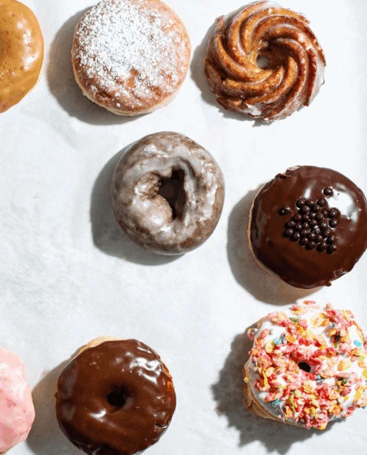 An assortment of eight decorated donuts, each with different glazes, sprinkles, and toppings, arranged on a white surface—perfect for sharing or celebrating New Year's Day from your favorite Birmingham restaurants open for the holiday.