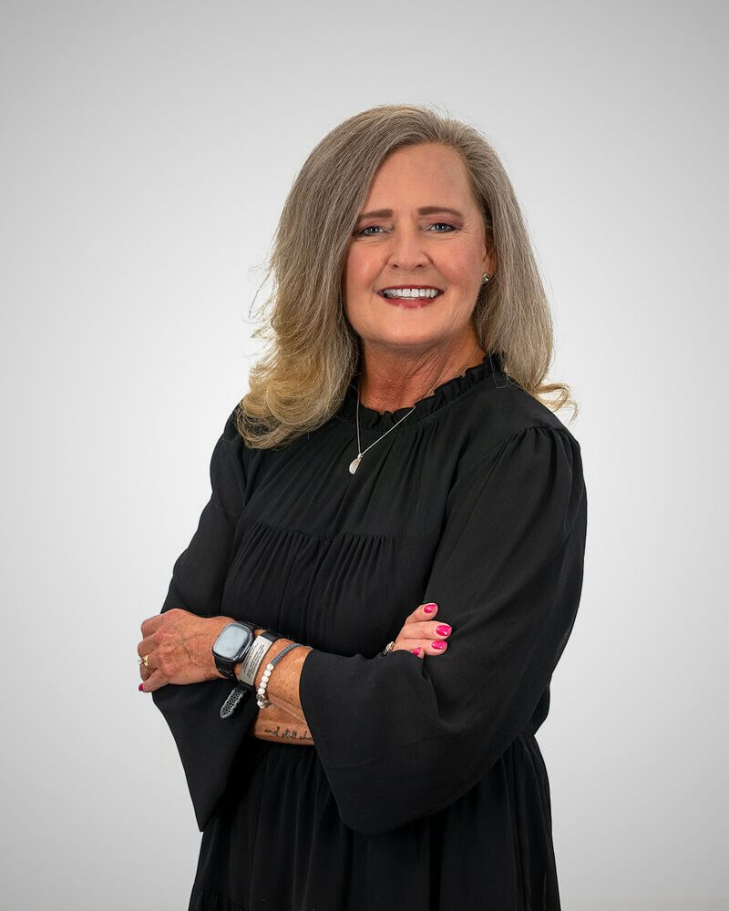Her Toy Drives Bring Joy & Relief to BHAM Families - 2 Doris Phillips, part of Birmingham FACES and Circle of Love, stands with arms crossed, smiling in her black dress and long gray hair against a plain light background.