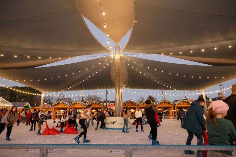 People ice skating under a large canopy decorated with string lights, surrounded by wooden market stalls and festive holiday decorations—a perfect Birmingham experience for those seeking unique gift experiences this season.