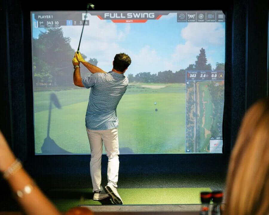 A man swings a golf club in front of a large golf simulator screen showing a virtual golf course—one of the top Birmingham experiences and perfect for unique Birmingham gifts or gift ideas.