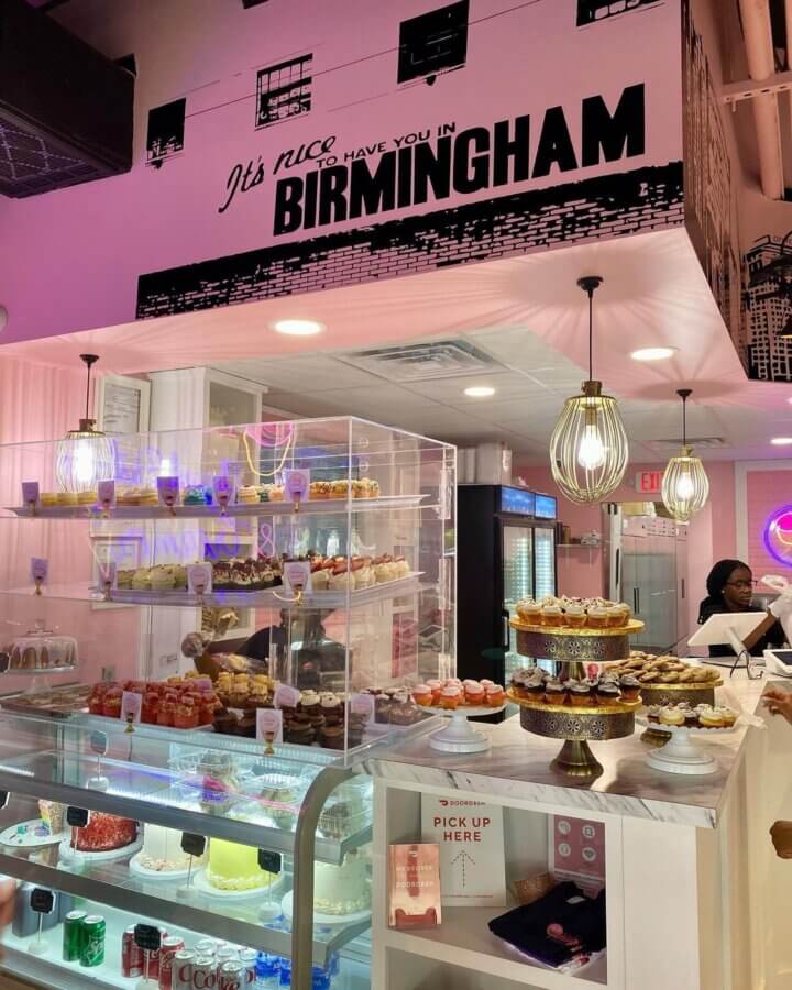 Meet Kristal Bryant of K&J’s Elegant Pastries & Creamery - 3 A bakery with glass display cases filled with cakes and cupcakes, under a sign reading “It’s nice to have you in Birmingham.” at K&J's Elegant Pastries.