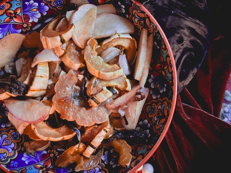 Cooking Unscripted: Roasted Delicata Squash with Apples & Sage - 2 A decorative bowl filled with sliced apples, roasted delicata squash, and onions sits on a patterned fabric surface.